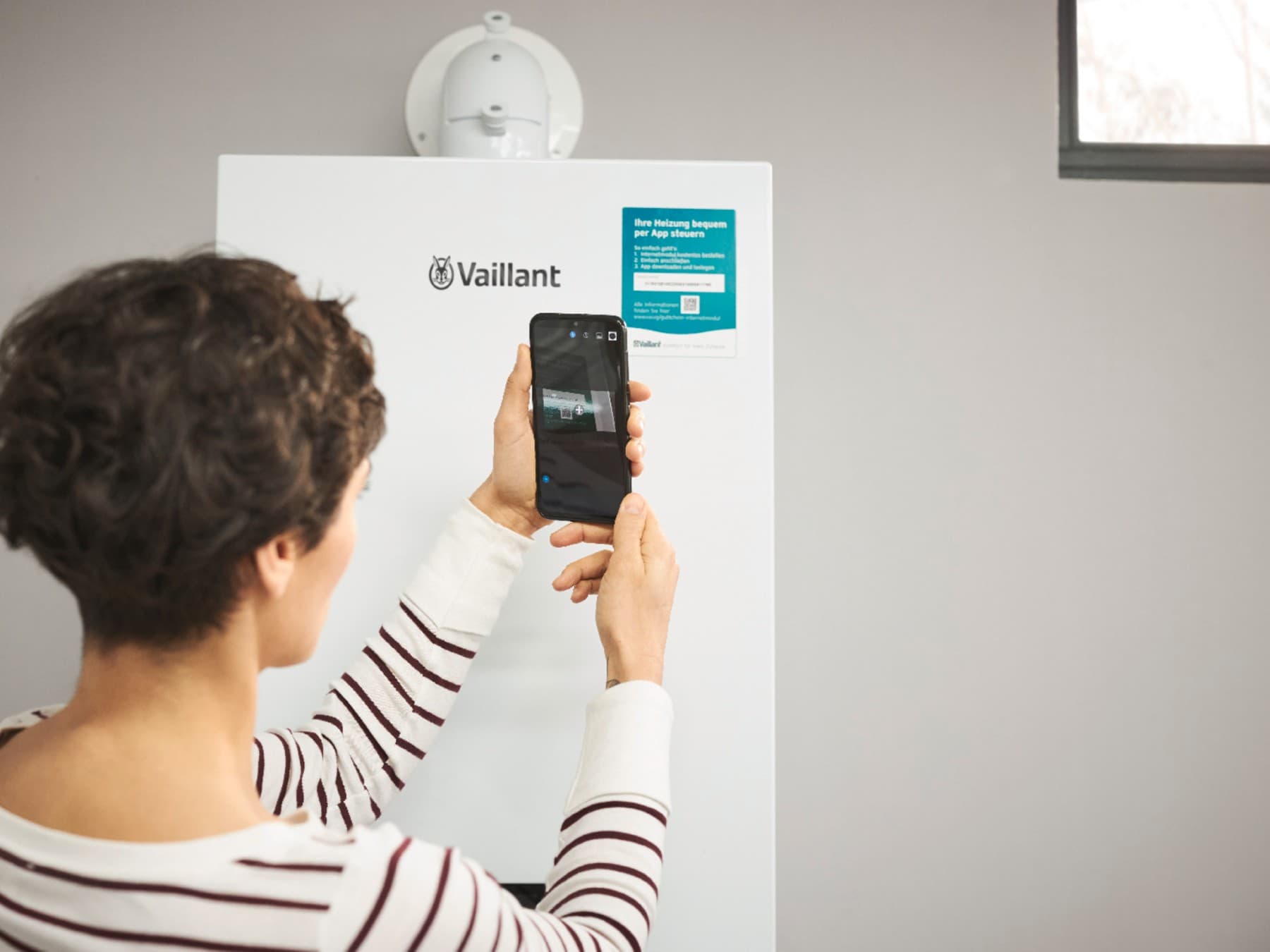 moteris savo išmaniuoju telefonu nuskenuoja QR kodą ant šildymo įrenginio